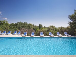 A swimming pool with clear blue water and white lounge chairs arranged along the edge.