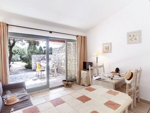 A cozy room with a dining table, chairs, a television, and a view of the garden through a sliding glass door.
