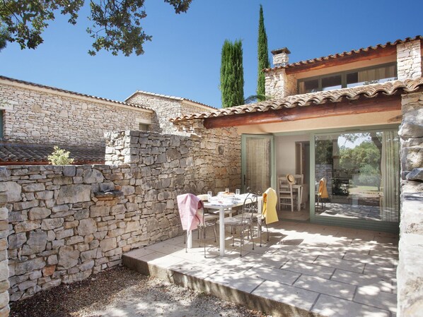 A stone building with a patio area featuring a table and chairs, a stone wall, and a view of the surrounding landscape.
