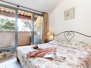 A bedroom with a bed, a window, a stone wall, a lamp, and a framed picture on the wall.