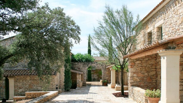 A stone pathway leading through a courtyard with buildings on either side, featuring arches and columns.