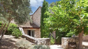 A stone building with a tiled roof, surrounded by various trees and shrubs.