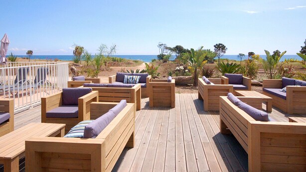 Une terrasse en bois avec des sièges extérieurs et une vue sur la plage.