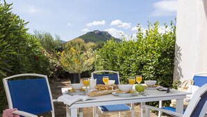 An outdoor dining area with a table set for breakfast, surrounded by chairs, and a view of a mountain in the background.
