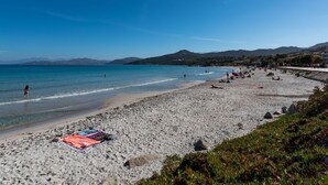 A beach with clear blue water, people sunbathing, and a colorful towel on the sand.