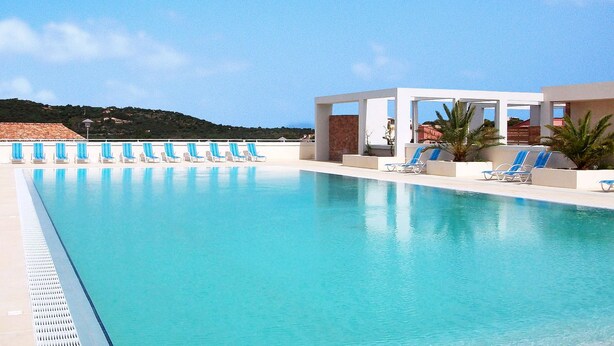 A swimming pool with lounge chairs and a covered area, surrounded by a clear sky and a hilly landscape. - Odalys Référence Les Villas Bel Godère by Interhome (Lozari)