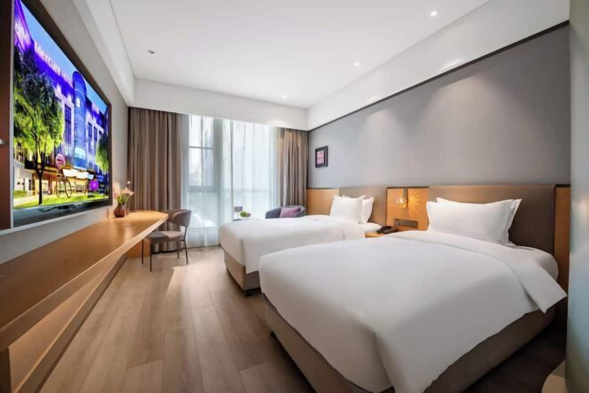 Habitación de hotel con dos camas, televisión, escritorio y ventana con cortinas.