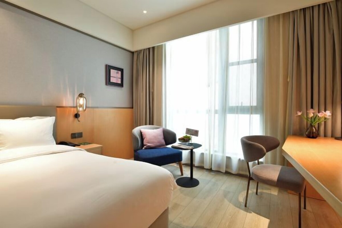 A hotel room with a large bed, a desk, a chair, and a small table.