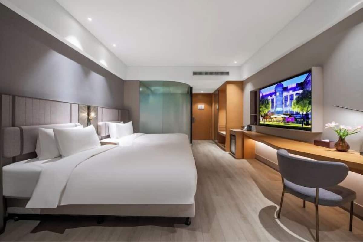 Habitación de hotel moderna con una cama grande, un escritorio y un televisor montado en la pared.