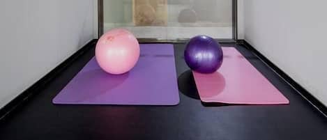 Dos pelotas de ejercicios sobre esterillas moradas en una habitación con pared de vidrio.