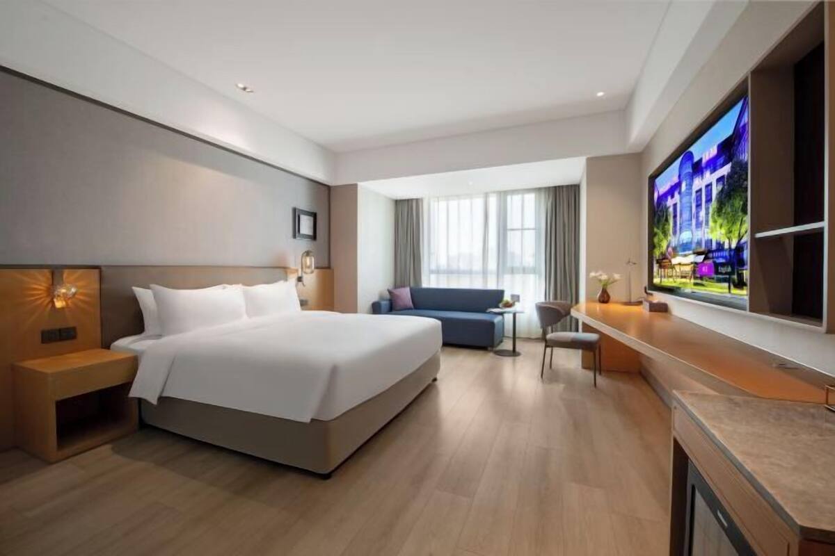 Una habitación de hotel moderna con una cama grande, un escritorio, un televisor y un sofá.