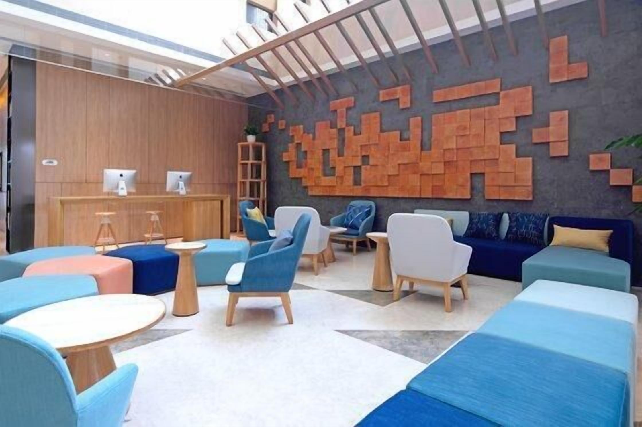 Un espace lounge moderne, doté de différents types de sièges, d’un comptoir d’accueil en bois et d’une œuvre d’art murale originale.