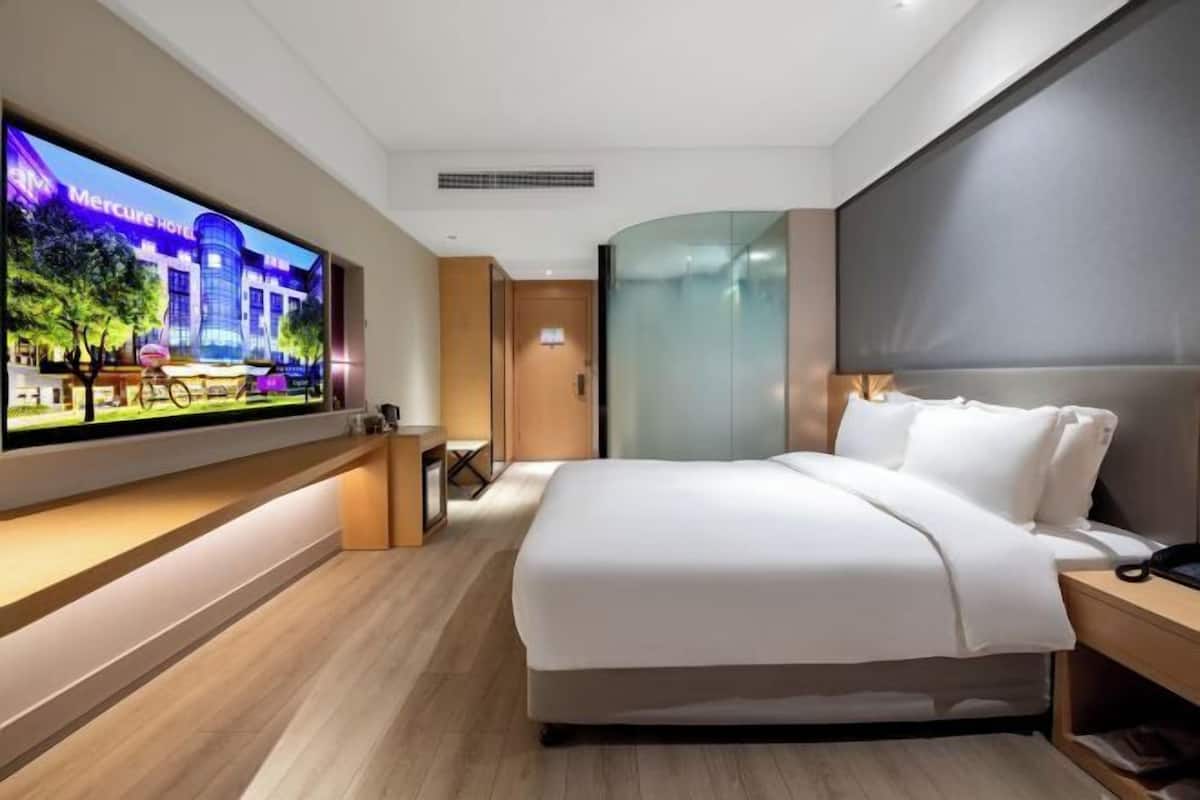 Habitación de hotel con una cama grande, un televisor de pantalla plana montado en la pared, piso de madera y un diseño moderno.