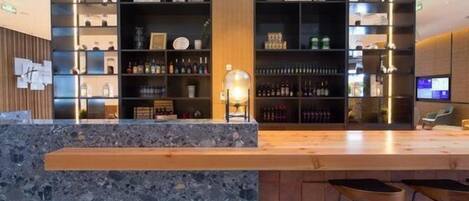 Zona de bar moderna con encimera de mármol, taburetes y estanterías llenas de botellas.