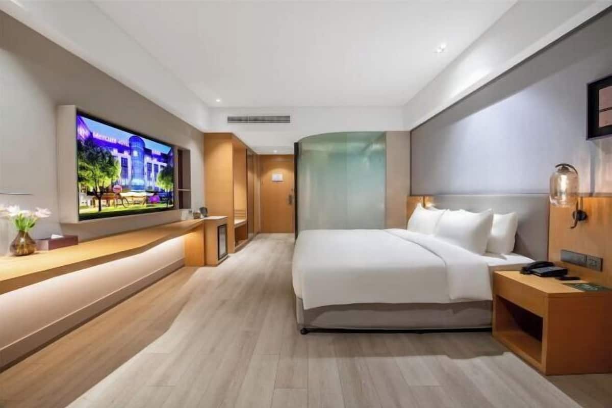 Una habitación de hotel moderna con una cama grande, un televisor montado en la pared, un escritorio de madera y una mesita de noche.