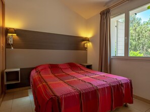 A hotel room with a bed, bedside tables, a window with curtains, and wall-mounted lamps.
