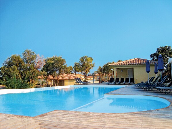 A swimming pool with lounge chairs and umbrellas, surrounded by trees and buildings with tiled roofs.