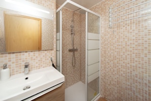 Ein Badezimmer mit Dusche, Waschbecken, Spiegel und gefliesten Wänden.