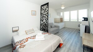 Ein Hotelzimmer mit Bett, Schreibtisch, Stuhl, Sofa, Raumteiler und Blick ins Freie.