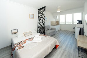 Une chambre d’hôtel comprenant un lit, un bureau, une chaise, un canapé, un paravent et une vue sur l’extérieur.