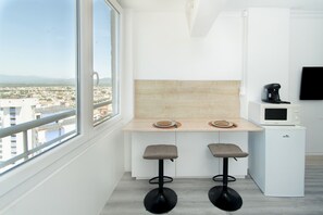 A modern kitchen with a large window, two bar stools, a microwave, and a small refrigerator. - WELCS ESTUDIO 178 EMP cerca del mar (Empuriabrava)