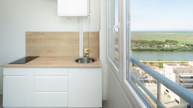 Eine kleine Küchenzeile mit einer Holzausstattung, einem Spülbecken und einem Fenster mit Blick auf einen Fluss und Gebäude.