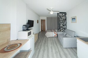 Ein Hotelzimmer mit einem Bett, einer Couch, einem Schreibtisch mit Computer, einem Fernseher und einem Deckenventilator.