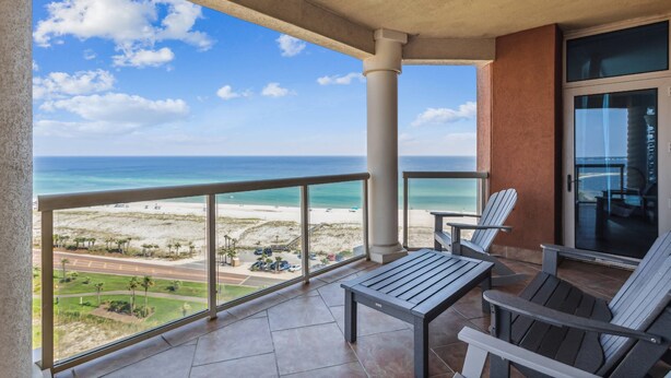 A balcony with a view of the beach and ocean, featuring a table and two chairs.