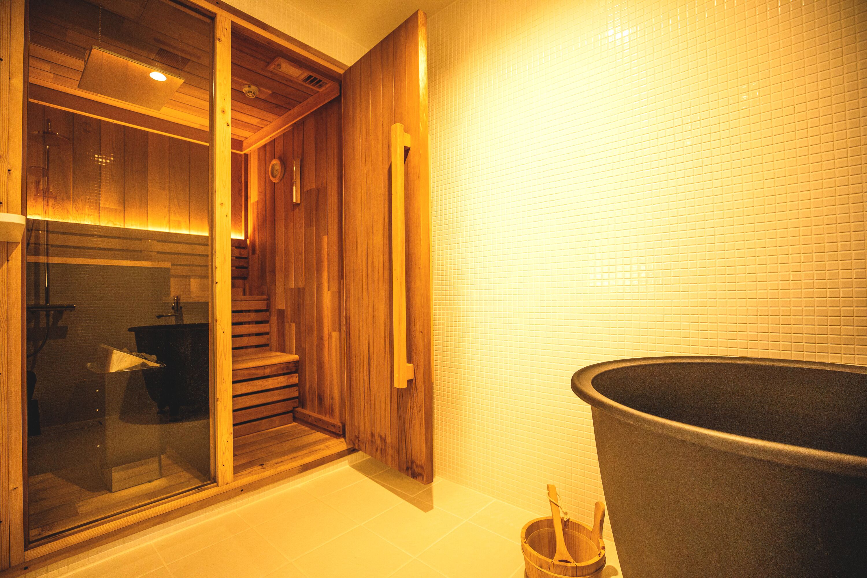 A wooden interior with a large black bathtub, wooden steps, and a glass door leading to a bathroom.