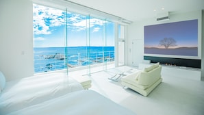 Quarto moderno com uma grande janela com vista para a costa, um sofá branco e uma lareira.