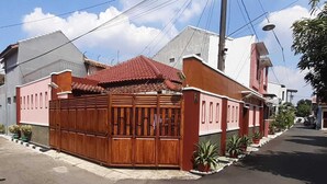 A residential house with a red-tiled roof, a wooden gate, and potted plants along the driveway. - Homestay Cendana Candi-1 (Kudus)