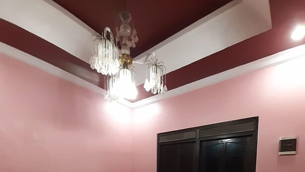 A room with a pink wall, a black window, and a chandelier. There are four chairs arranged in the room. - Homestay Cendana Candi-1 (Kudus)