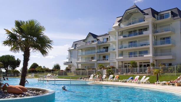 Un hotel con piscina, varios balcones y un césped bien cuidado.