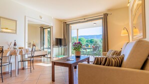 Een ruime woonkamer met een groot raam dat uitzicht biedt op een prachtig landschap, een eethoek met een tafel en stoelen, en een gezellige zithoek met een bank.