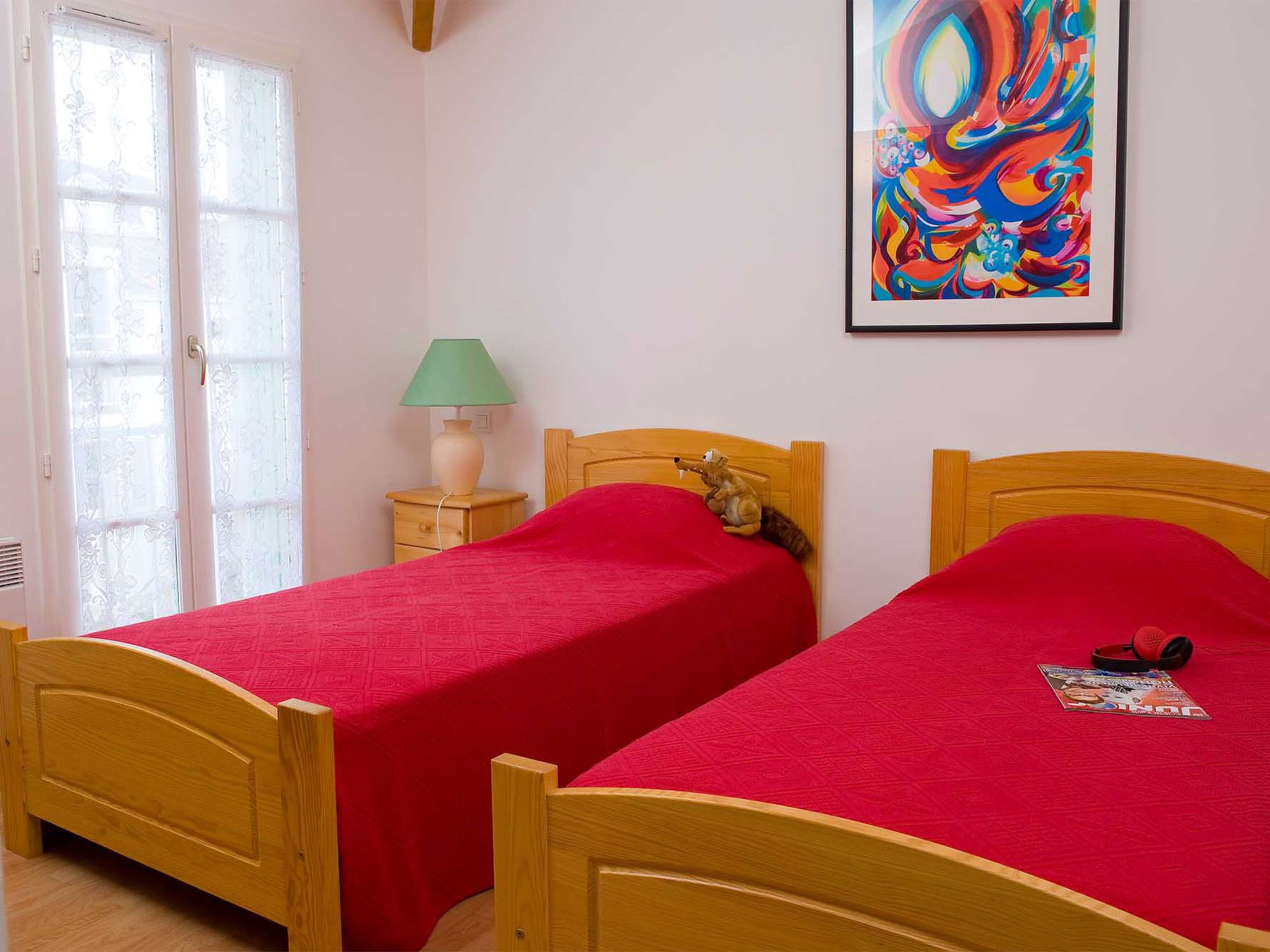 A bedroom with two wooden beds, a green lamp, a squirrel figurine, and a colorful abstract painting on the wall.