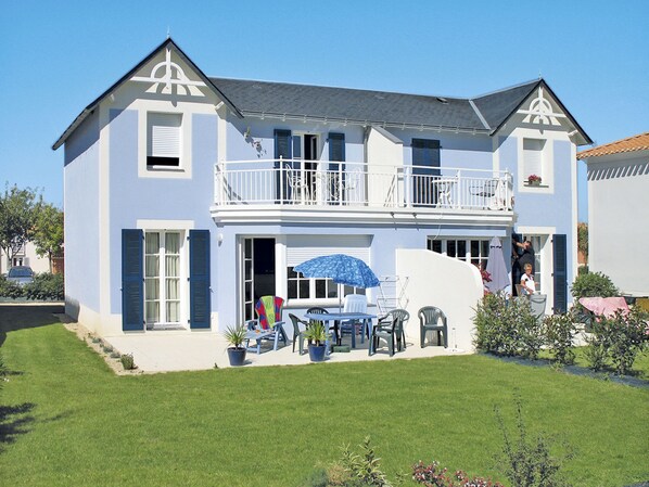 Ein zweistöckiges Haus mit Balkon, einer Terrasse und Gartenmöbeln sowie einem gepflegten Rasen.
