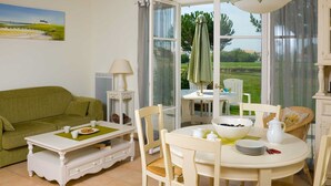 A dining area with a white table and chairs, a bowl of fruit, and a green umbrella.