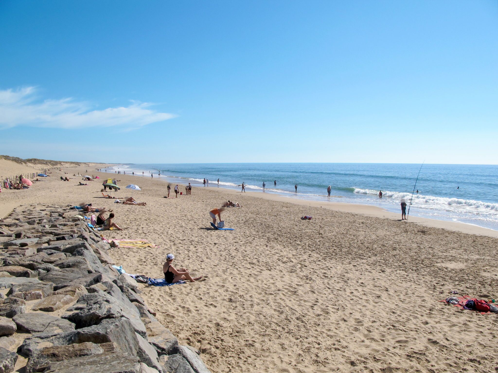 A beach with people sunbathing and swimming, a rocky shoreline, and a clear sky.