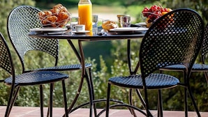 A table set outdoors with breakfast items, including croissants, fruit, and juice, with chairs and a scenic view in the background. - Provence Country Club by Interhome (L'isle sur la Sorgue)