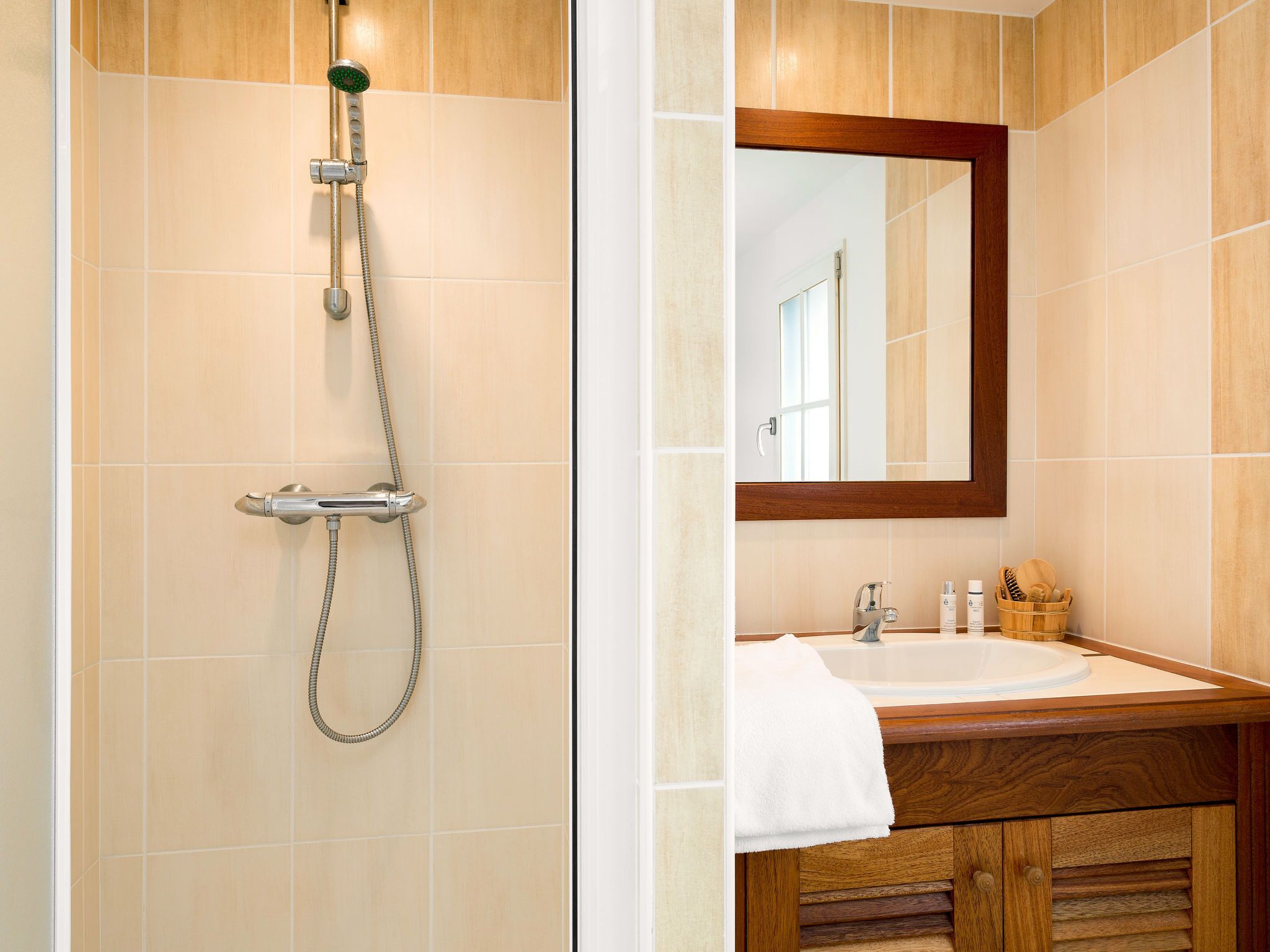 Een badkamer met een douche, wastafel en een houten wastafelmeubel.