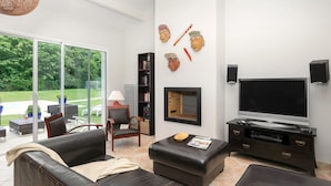 A modern living room with a large TV, comfortable seating, a bookshelf, and a view of the outdoors.