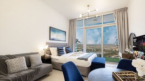 Een moderne hotelkamer met een groot raam, een bed met blauw-witte beddengoed, een grijze bank, een blauwe fauteuil en een klein tafeltje met chocolade.
