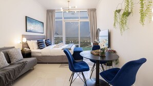 Een moderne slaapkamer met een groot raam, een bed, een bank, een eettafel en blauwe stoelen.