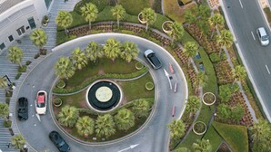 Een cirkelvormige weg met palmbomen en een centrale fontein, omringd door groen en gebouwen.