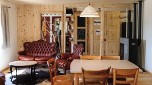 Ein Holzinterieur mit einem Esstisch, Stühlen, einem Ledersofa und einer Deckenleuchte.