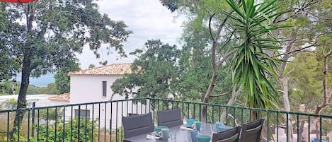 A patio with a table and chairs, a red umbrella, and a view of a building and trees.