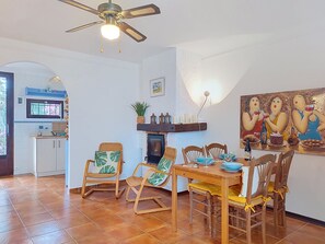 Ein Essbereich mit Holztisch und -stühlen, einem Deckenventilator, einem Kamin und einem Gemälde an der Wand.