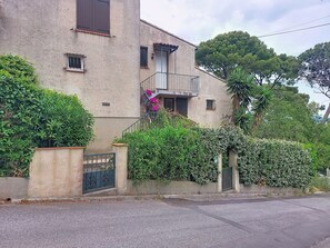 A two-story building with a balcony, a gated entrance, and lush greenery.