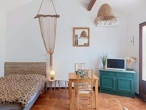 Ein Zimmer mit einem Bett, einem Esstisch mit Stühlen, einem Fernseher auf einer Kommode und einer Hängelampe.