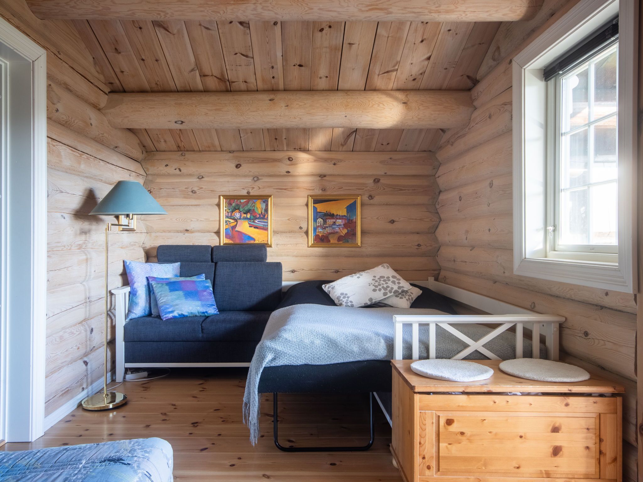 A cozy cabin room with a wooden interior, a sofa, a small table, and a floor lamp.